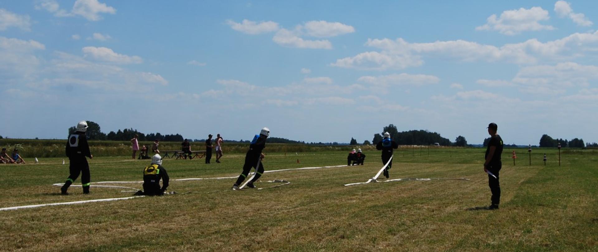 Zawody Sportowo – Pożarnicze jednostek OSP z terenu gmin Sterdyń i Sabnie 2022 - na zdjęciu strażacy w ubraniu koszarowym rozwijają linie i je łączą.