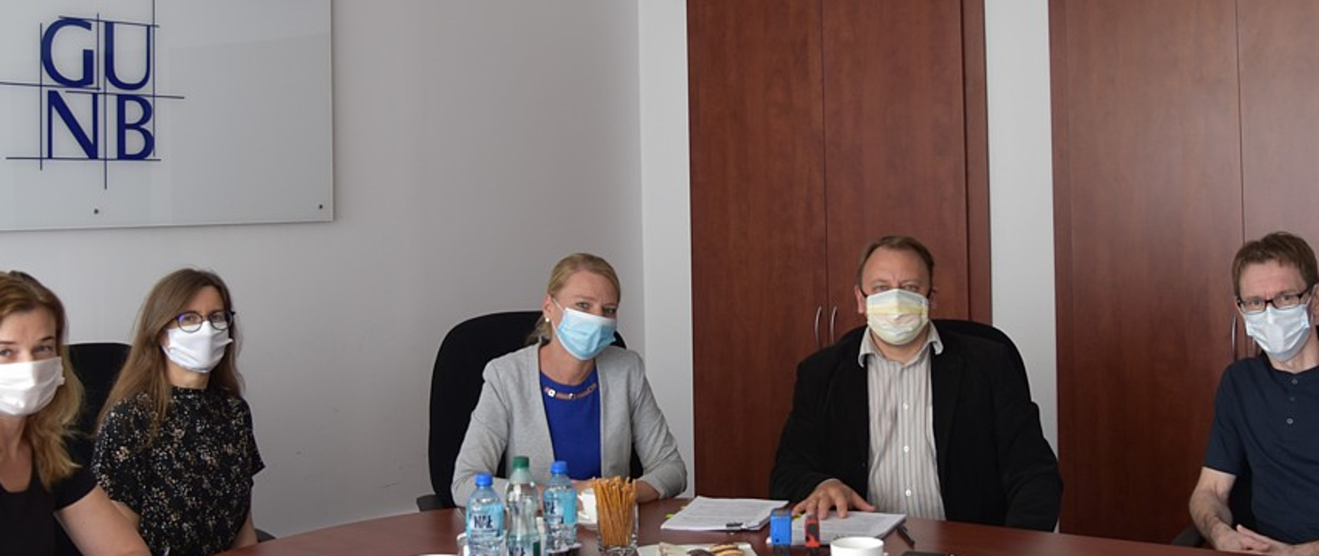 Pięć osób w maseczkach siedzących przy stole w sali konferencyjnej podczas podpisania umowy
