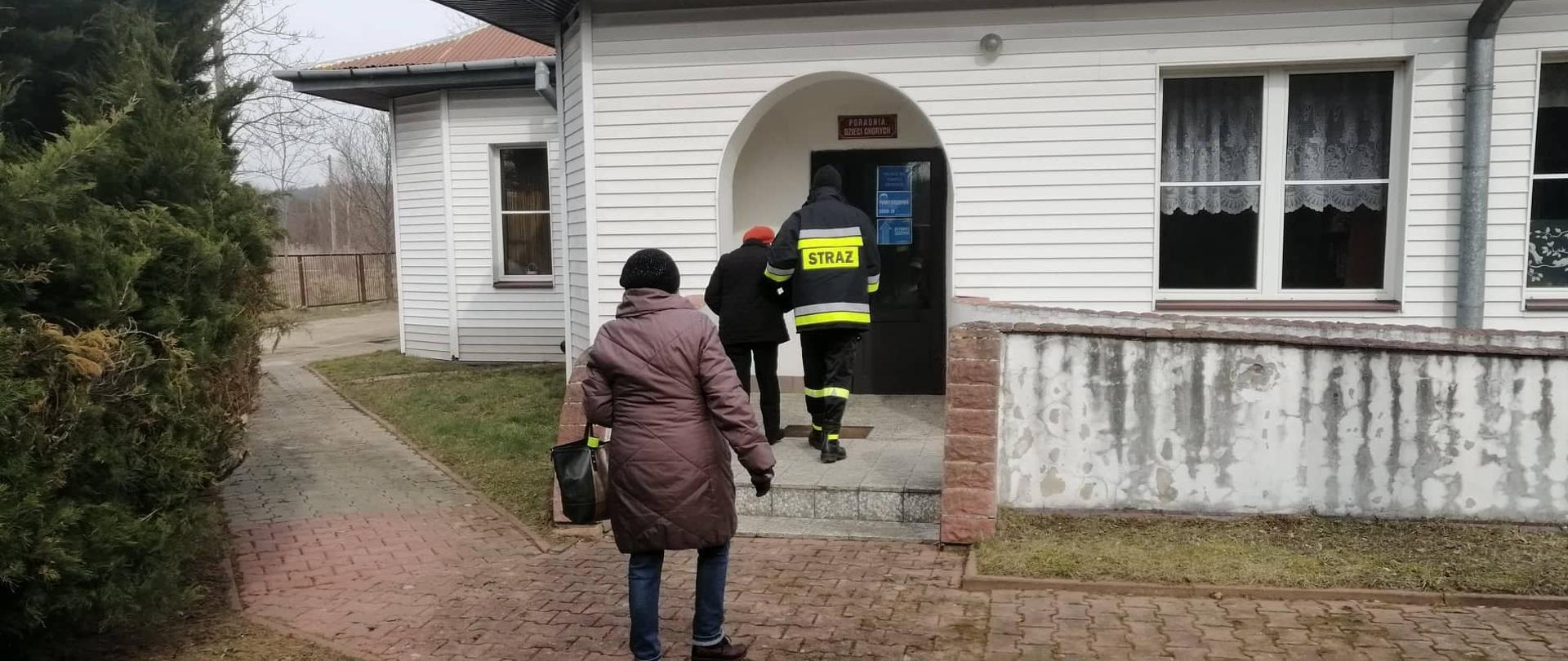 Strażak prowadzi starszą kobietę do punktu szczepień 11 marca 2021r