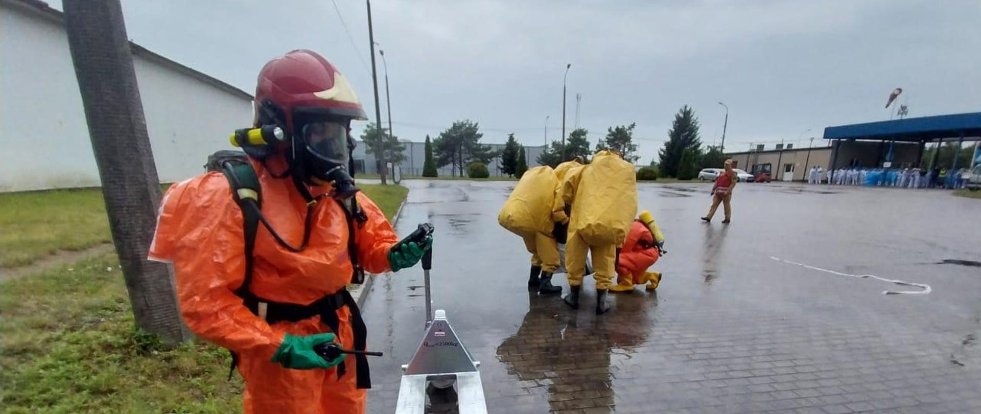 Ratownik w ubraniu przeciwochlapaniowym a w tle ratownicy w ubraniach gazoszczelnych