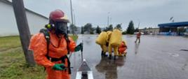 Ratownik w ubraniu przeciwochlapaniowym a w tle ratownicy w ubraniach gazoszczelnych