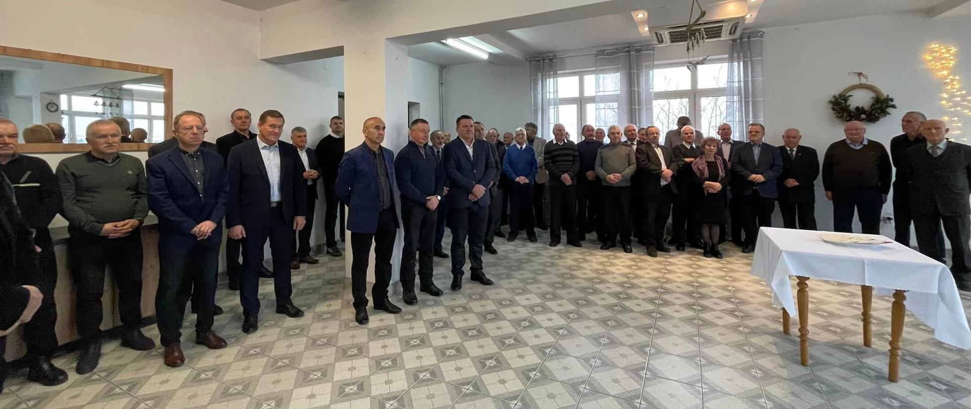 Emeryci i renciści stoją na sami a na środku stół z opłatkami.