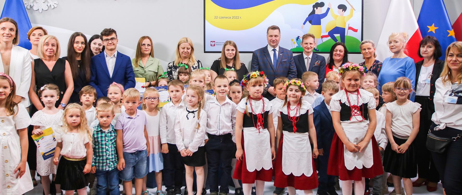 Zdjęcie zbiorowe, duża grupa dzieci stoi pod ścianą, na której jest napis Dobry obywatel.