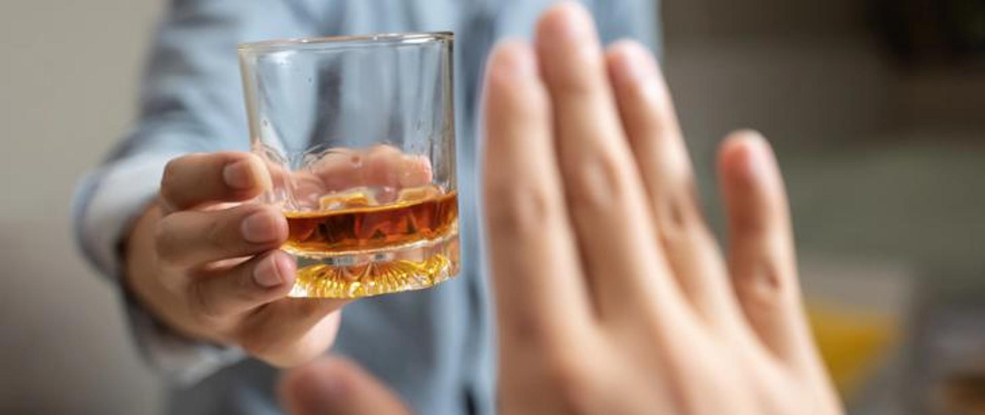 Zdjęcie przedstawia osobę, która odmawia wypicie alkoholu. 