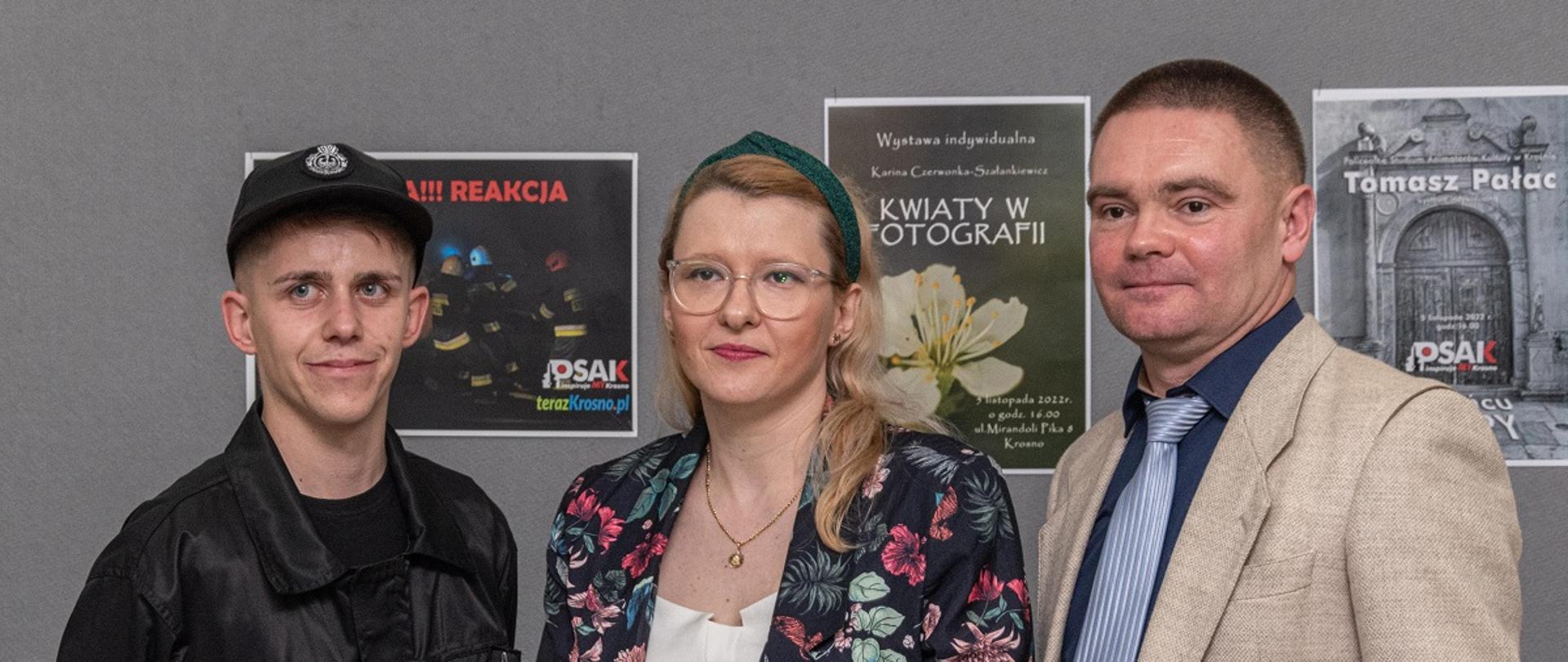  Zdjęcie przedstawia trójkę słuchaczy Studium podczas swoich wystaw fotograficznych. Stoją na tle swoich plakatów zapowiadających wystawy.