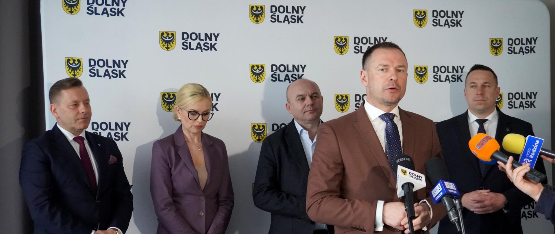 Konferencja prasowa Piotra Borysa we Wrocławiu na temat strategii rozwoju turystyki w Polsce i na Dolnym Śląsku. Minister stoi na tle ścianki z logiem Dolnego Śląska oraz za mikrofonami