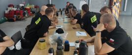 grupa strażaków siedi przy długi mstole , na stole znajdują się środki chemiczne