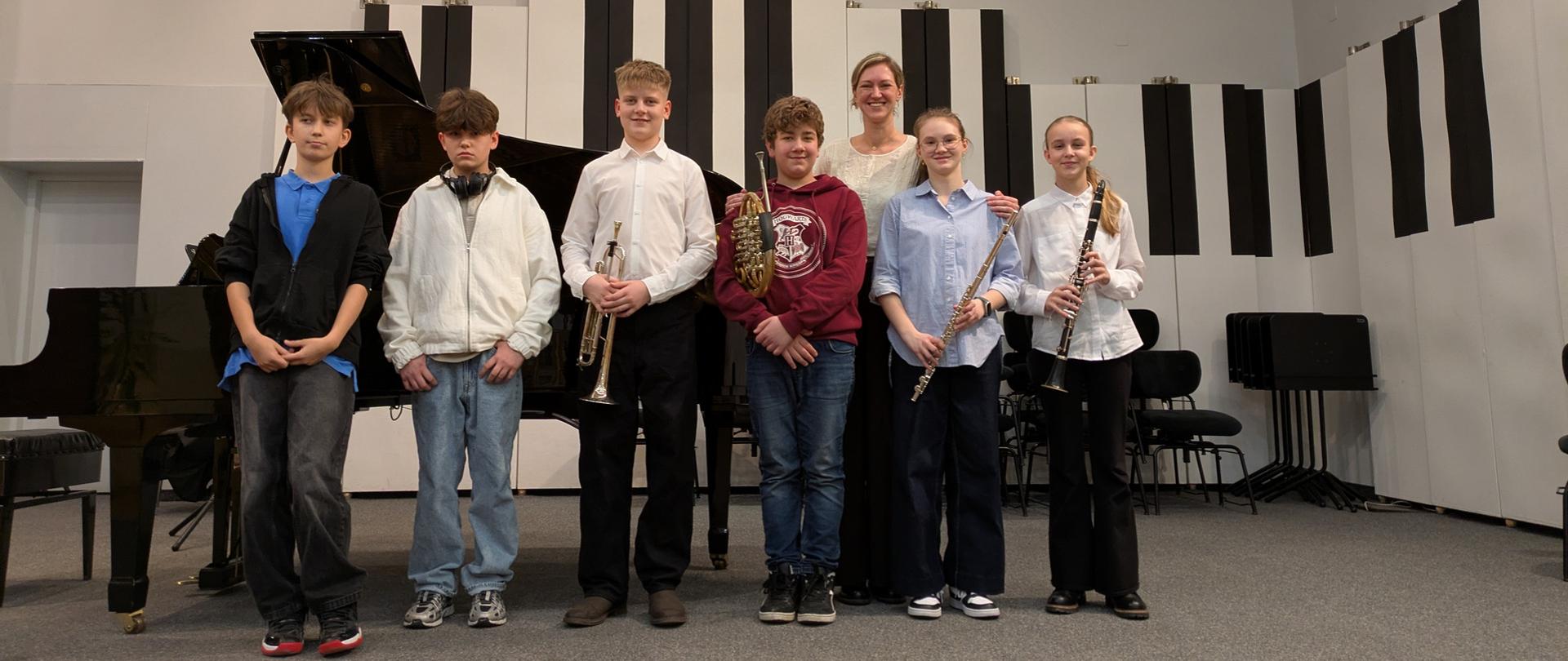 Wszyscy wykonawcy stoją z nauczycielką na scenie.