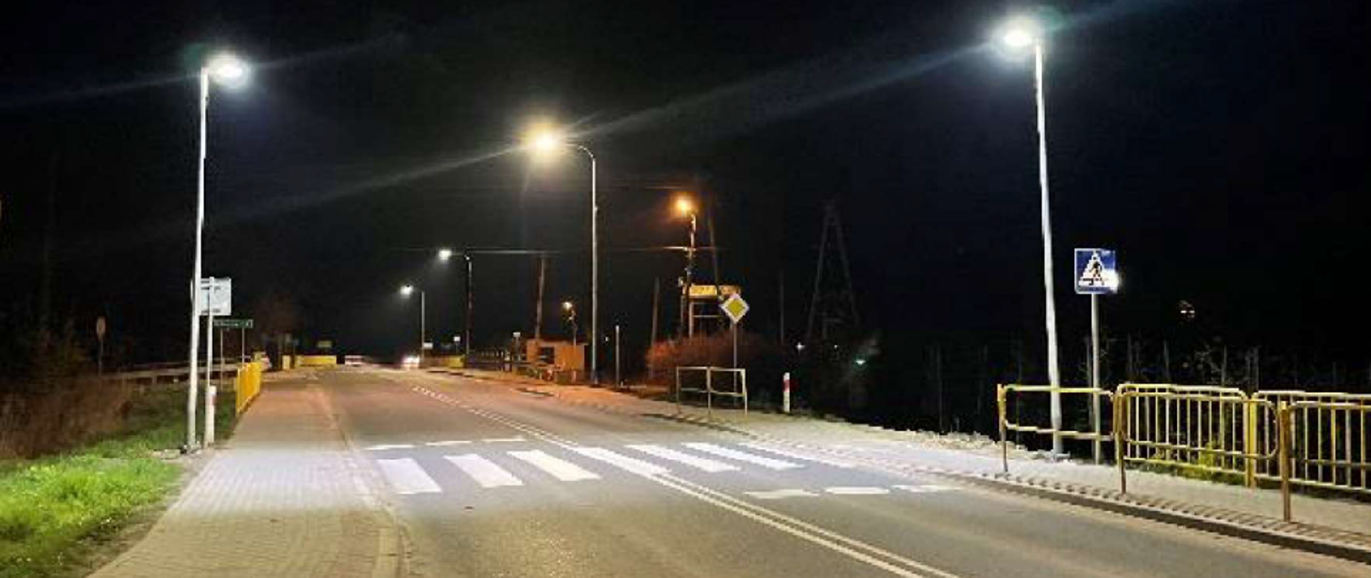 Przejście dla pieszych z dodatkowym oświetleniem - zdjęcie nocne, droga, po obu stronach chodniki, przejście dla pieszych, po obu stronach przejścia latarnie rzucające światło dokładnie na pasy dla pieszych