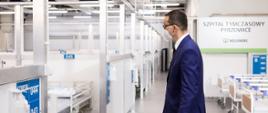 Premiera Mateusz Morawiecki idzie po korytarzu nowego szpitala tymczasowego w Pyrzowicach. W tle puste łóżka.