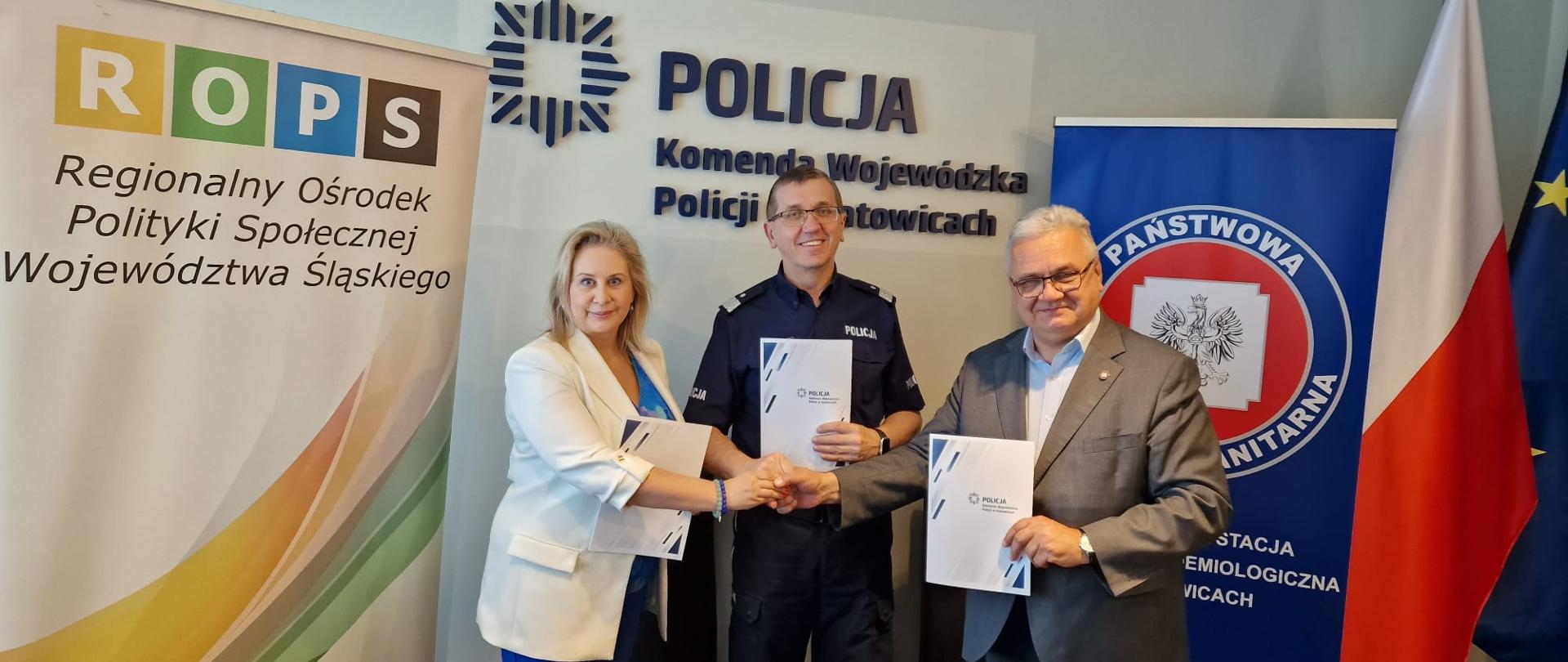 Trzech Partnerów Regionalnej Koalicji na rzecz przeciwdziałania uzależnieniu, w tle bannery trzech Instytucji - Regionalny Ośrodek Polityki Społecznej Województwa Śląskiego, Komenda Wojewódzka Policji w Katowicach, Wojewódzka Stacja Sanitarno-Epidemiologiczna w Katowicach
