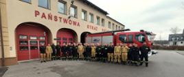 Zdjęcie grupowe uczestników szkolenia - strażaków, po zakończonym egzaminie na tle budynku KP PSP w Kartuzach oraz wozu strażackiego.