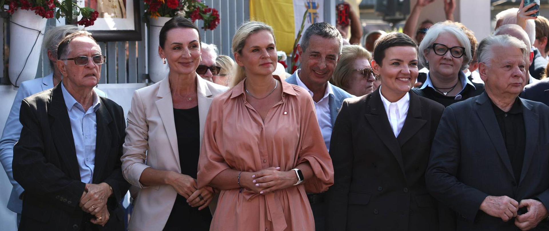 kilka osób stoi przed brama stoczni, w tle portret Papieża św. Jana Pawła II