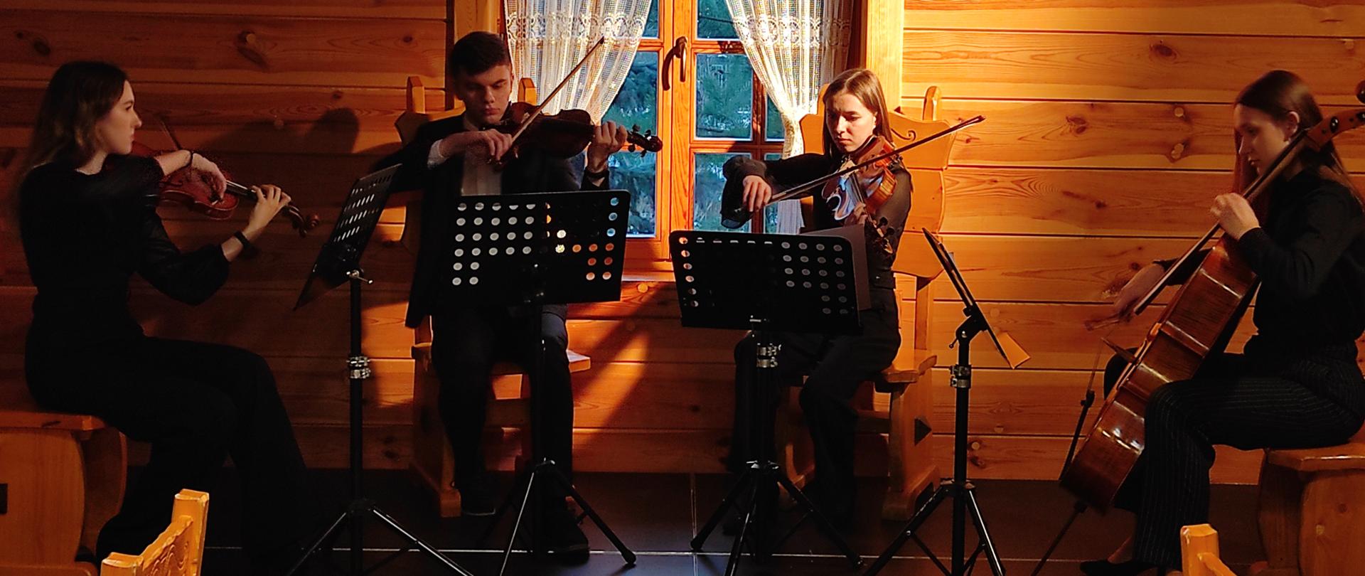 zdjęcie przedstawia kwartet smyczkowy Państwowej Szkoły Muzycznej na uroczystej kolacji wigilijną zorganizowaną dla wszystkich pracowników ITA TOOLS w Karczmie Polskiej na tle okna i drewnianych ścian