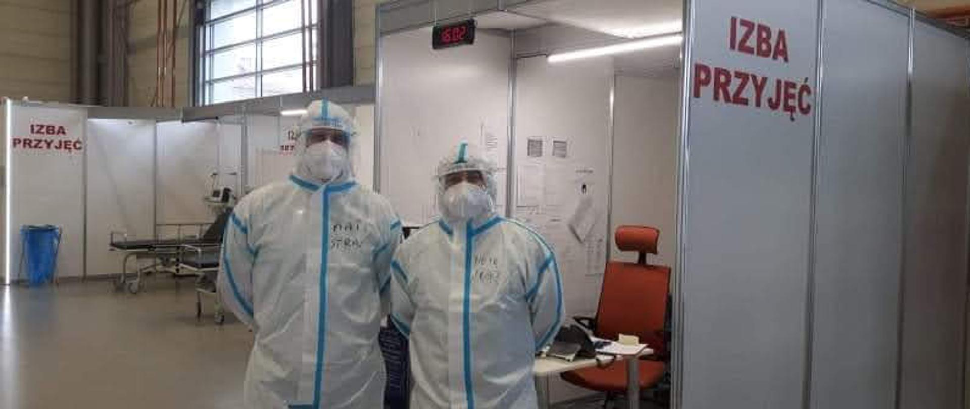 FUNKCJONARIUSZE KP PSP W KROTOSZYNIE W UBRANIACH OCHRONNYCH NA TERENIE SZPITALA TYMCZASOWEGO ZLOKALIZOWANEGO NA TARGACH POZNAŃSKICH. PO PRAWEJ WIDOCZNY NAPIS IZBA PRZYJĘĆ.