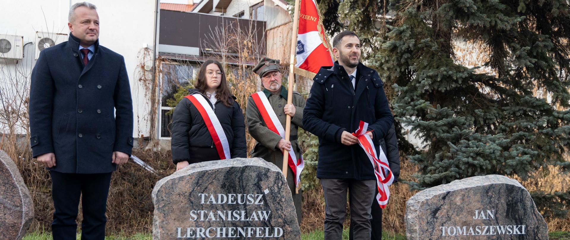
Grupa ludzi stojąca przy kamiennych tablicach upamiętniających bohaterów Powstania Wielkopolskiego
