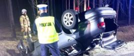 Widać samochód na dachu, w rowie, jest ciemno, w pobliżu Policjant i Strażaka