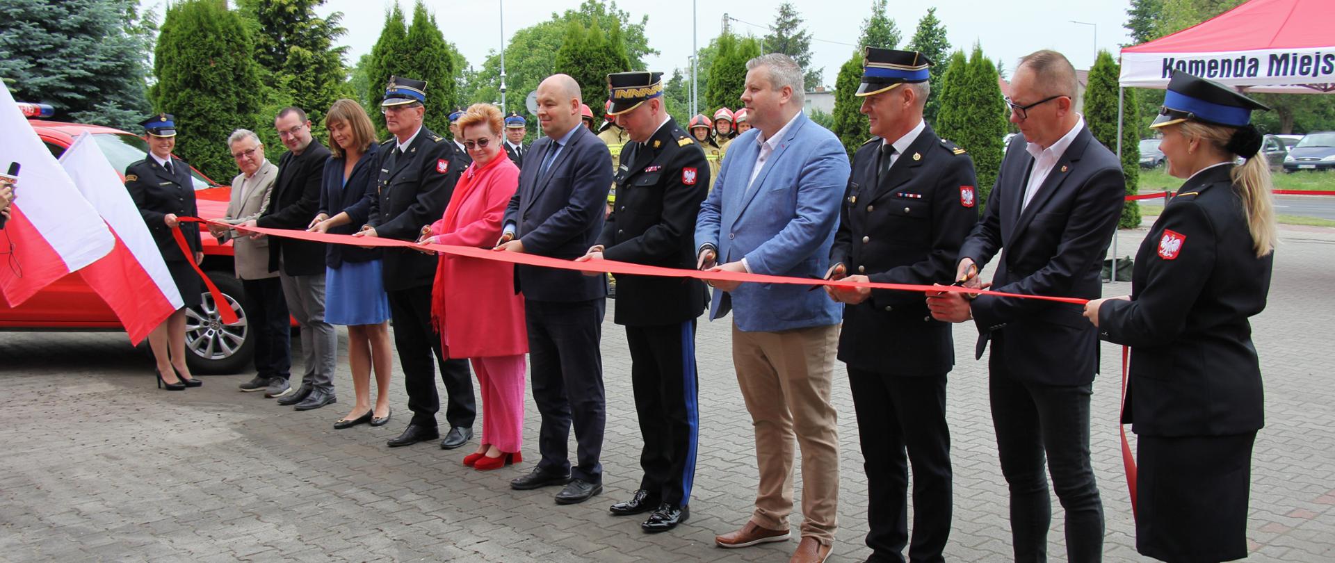 Osoby w mundurach i po cywilnemu przecinają szarfę.