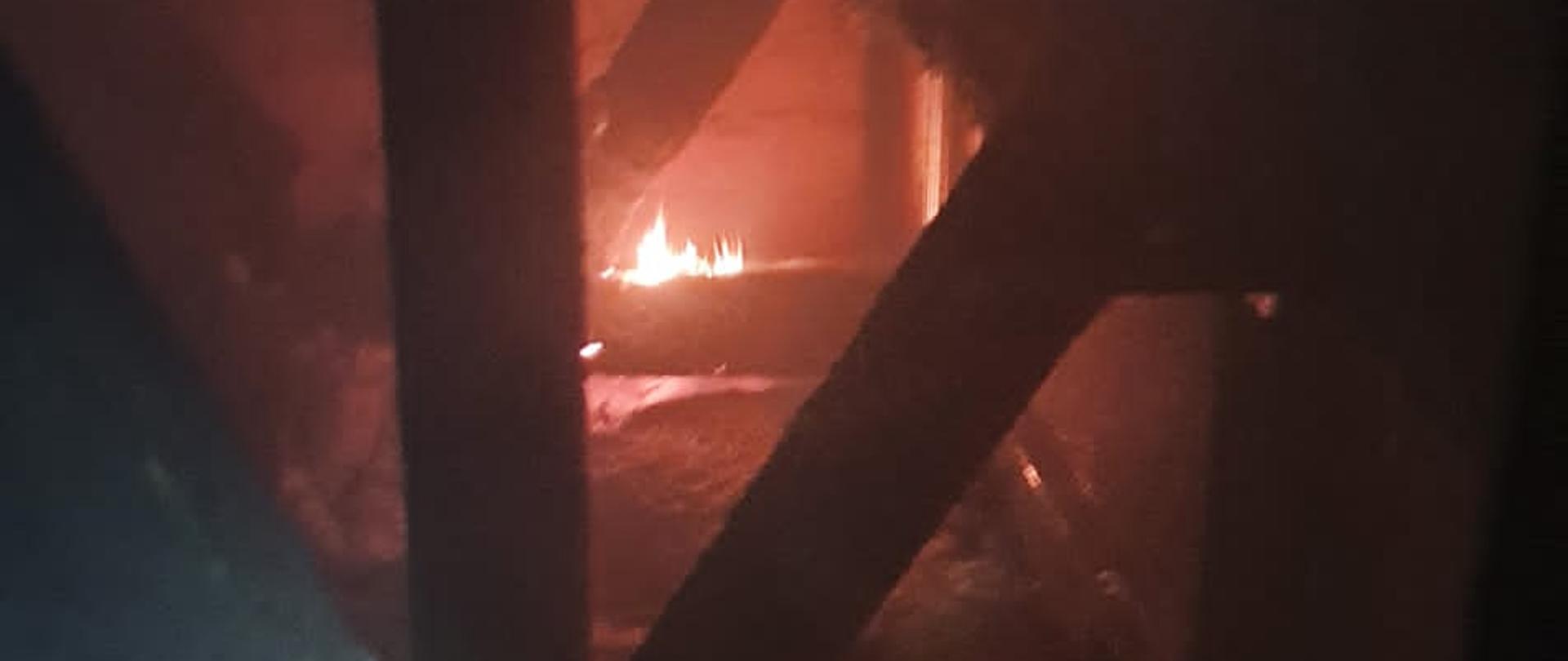 na zdjęciu konstrukcja drewniana poddasza z widocznym płomieniami jednej z belek z koku oświetlenie z latarki