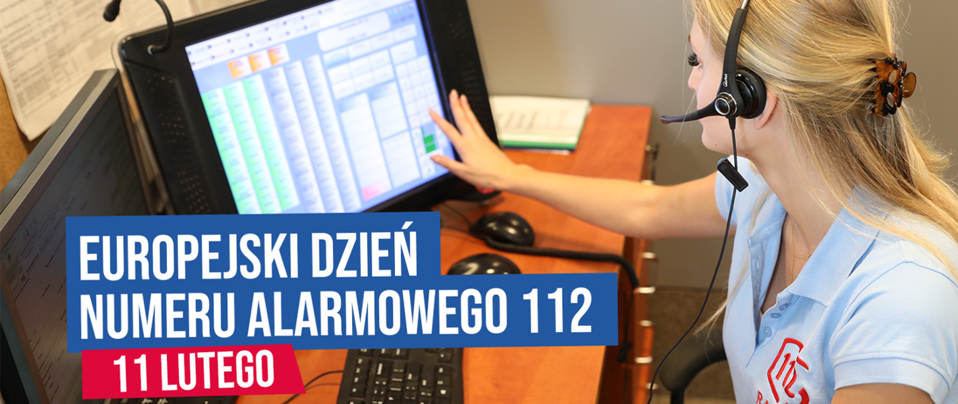 Dyspozytorka numeru alarmowego 112 siedzi przy biurku przed ekranem, palcami prawej ręki dotyka ekranu pulpitu dyspozytorskiego.