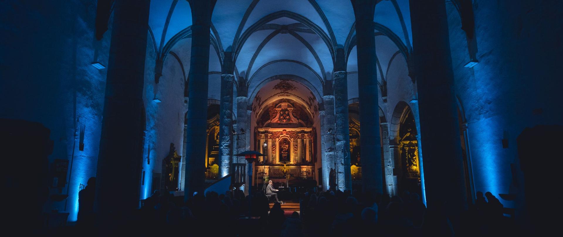 A Igreja Matriz em Arronches, onde um numeroso público se reuniu para o concerto do Zarębski Piano Duo. A abóbada da igreja está iluminada de azul. No fundo vê-se o altar iluminado.
