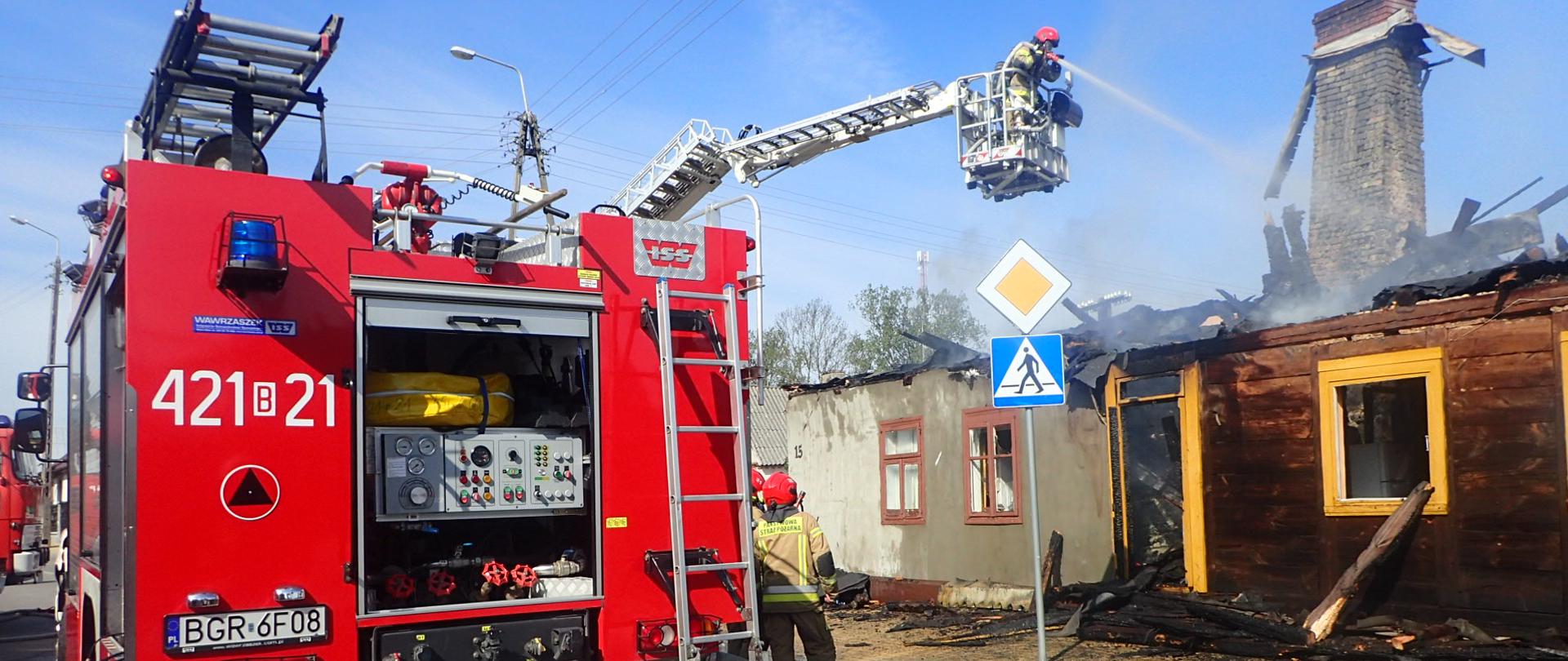 Samochód gaśniczy a w tle kosz SHD ze strażakami gaszącymi pożar.