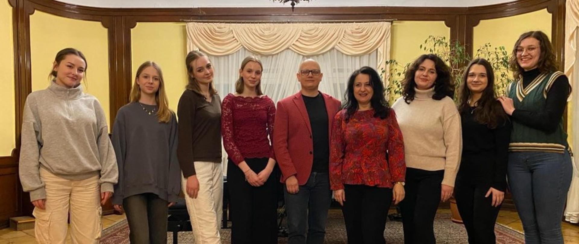 Zdjęcie kolorowe. Prof. Magdalena Witczak i mgr. Przemysław Sysojew - Osiński w otoczeniu grupy uczennic na scenie,