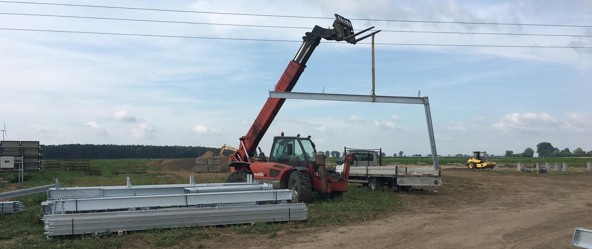 Na zdjęciu ładowarka teleskopowa unosząca element konstrukcji stalowej z wysuniętym ramieniem roboczym, które zahaczyło o napowietrzne linie energetyczne średniego napięcia.
