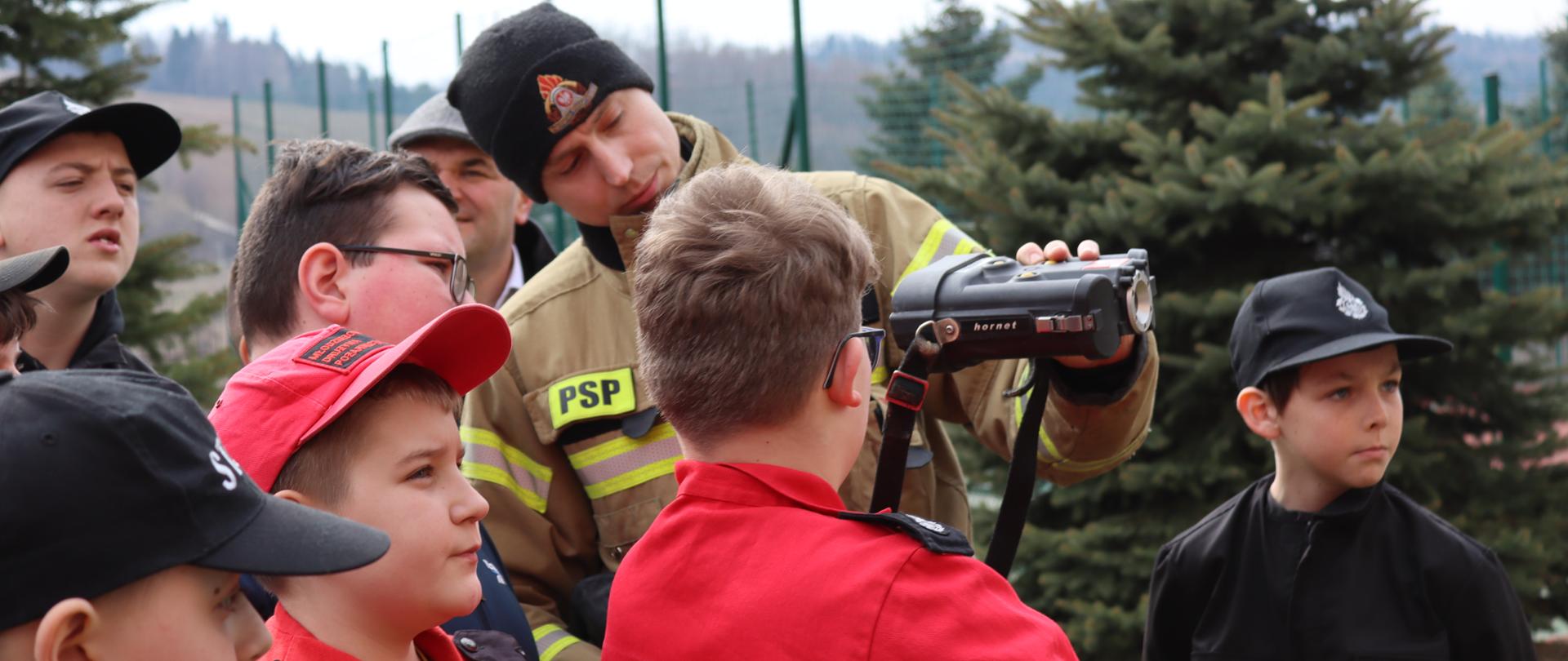 Strażak PSP prezentuje członkom MDP kamerę termowizyjną.