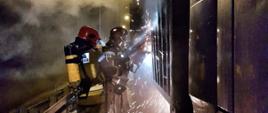 Zdjęcie przedstawia strażaków wycinających otwory w ścianie kontenera, które umożliwią podanie wody i ugaszenie ognia
