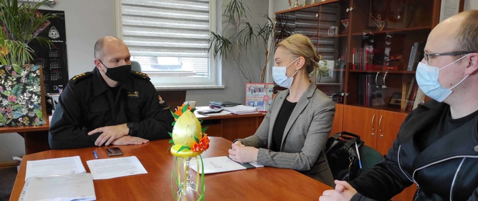 Na zdjęciu widać siedzących od lewej" komendanta powiatowego PSP w Oławie, Annę Imielską i Radosława Łączkowiaka z kliniki Harmony Clinic, podczas rozmowy.