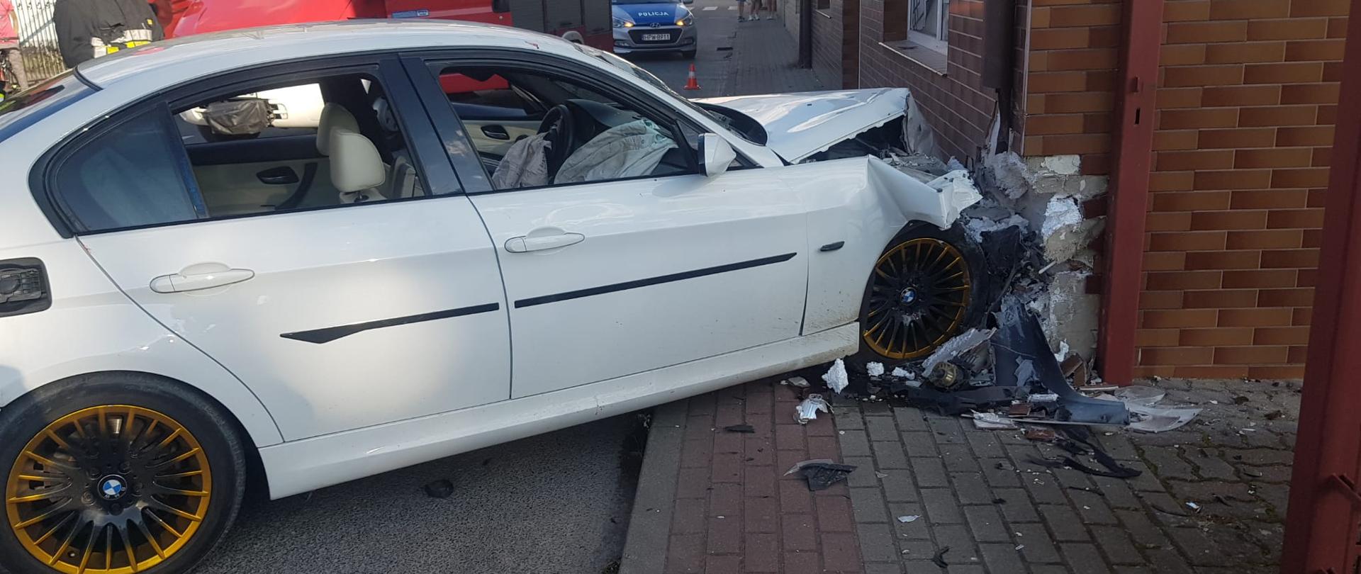Zdjęcie przedstawia biały samochód osobowy marki BMW, który uderzył w róg budynku.