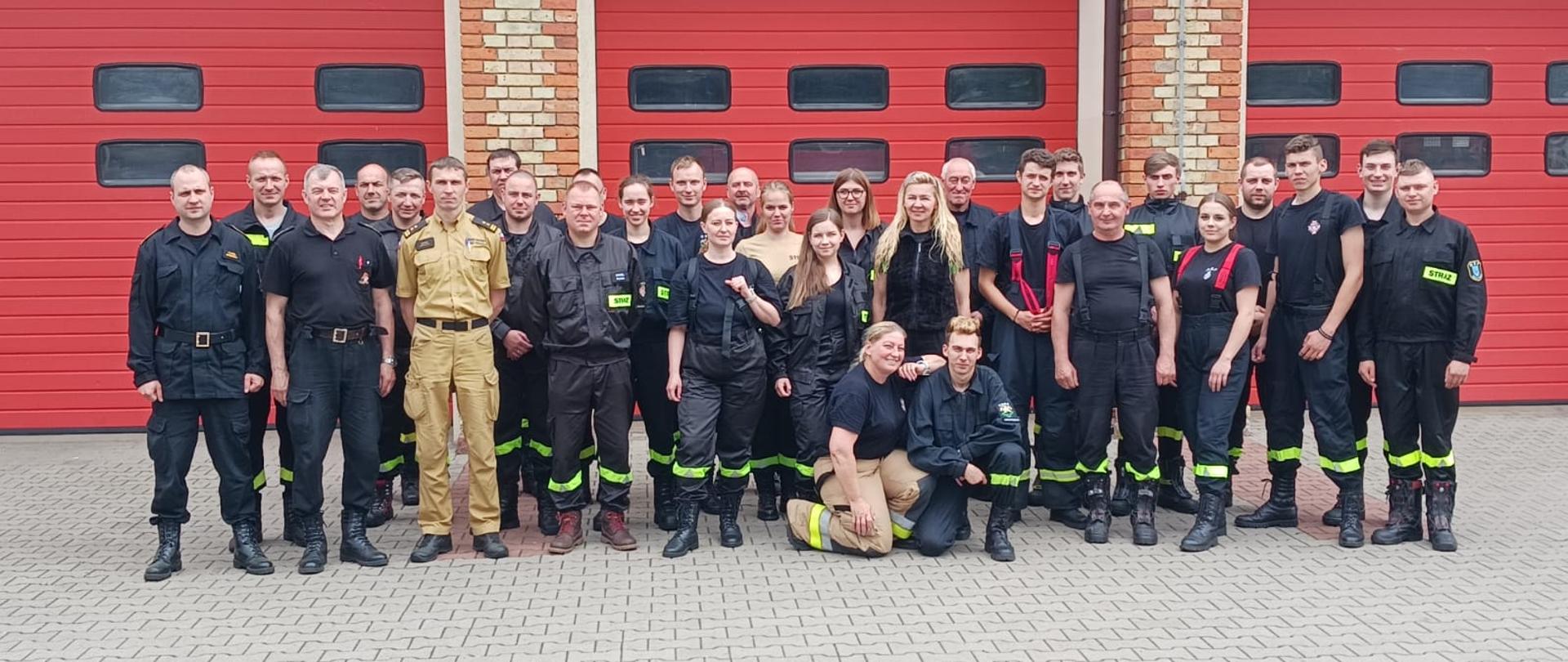 Zdjęcie grupowe uczestników szkolenia. W tle czerwone bramy garażowe.