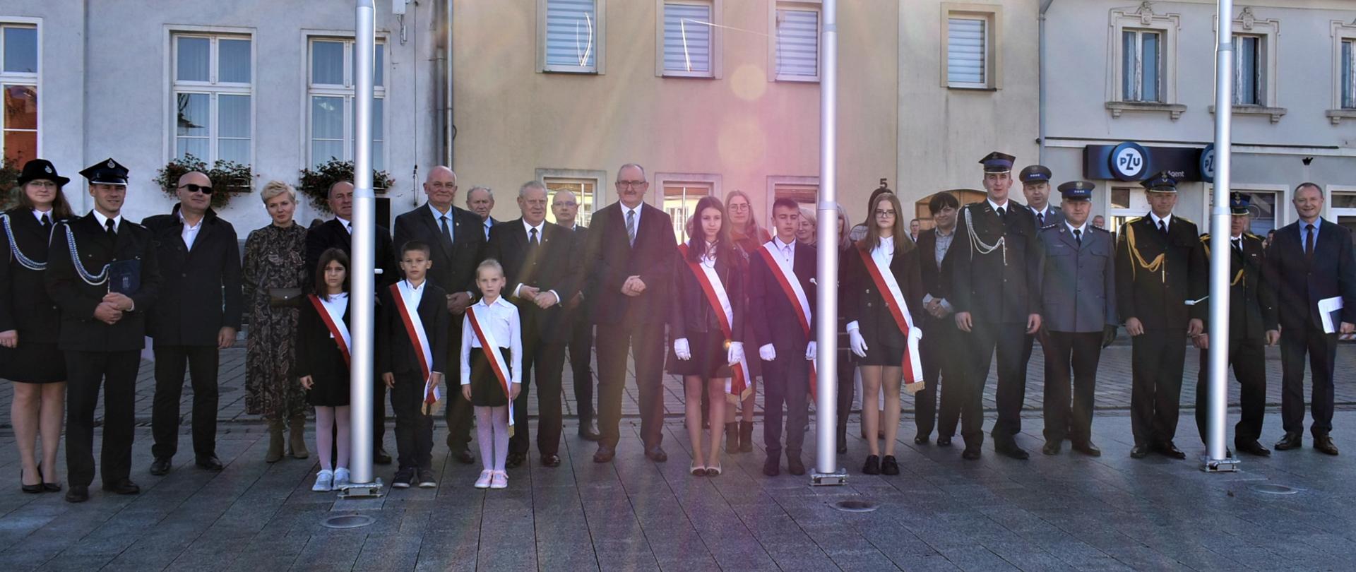 Grupa ludzi stojąca przed budynkami na rynku w Korfantowie