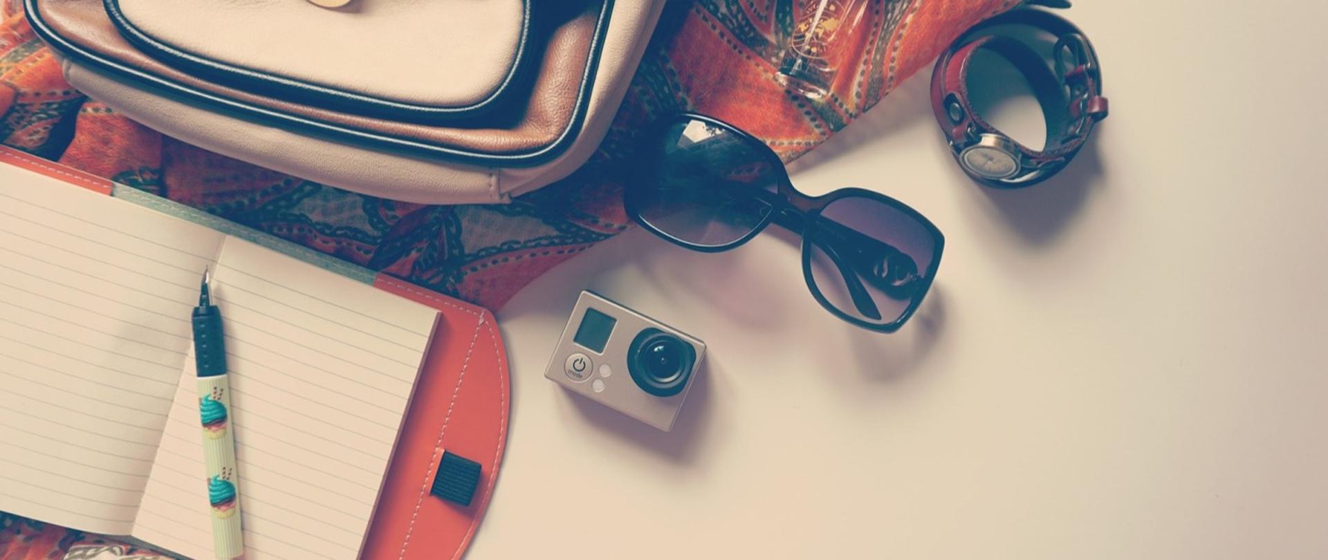 Grafika przedstawia książkę, długopis, okulary, kamerę, plecak, zegarek