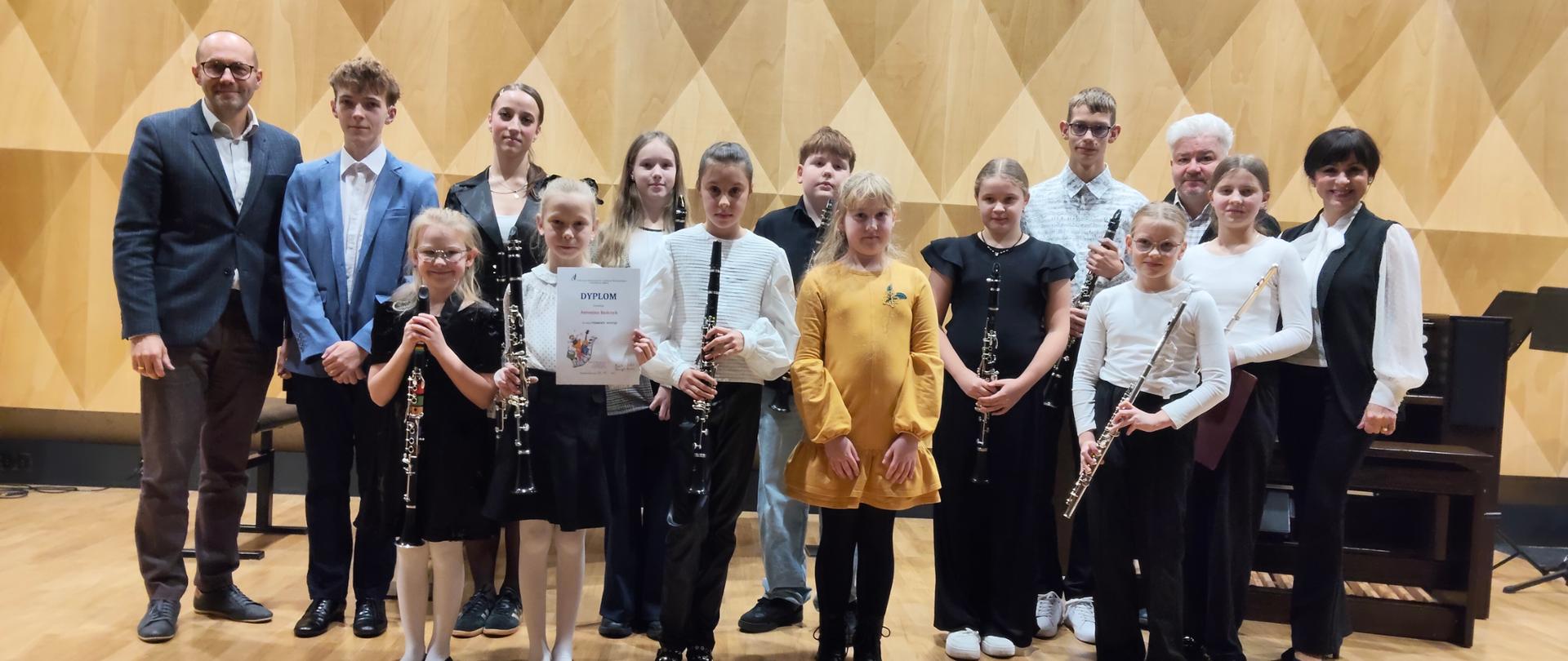 Grupa uczniów z klarnetami na scenie sali koncertowej