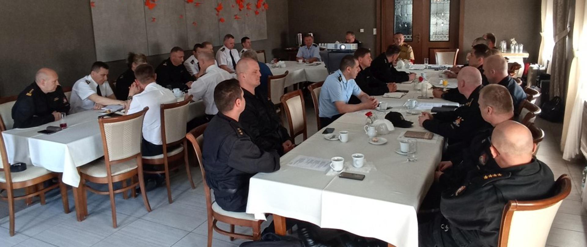 Funkcjonariusze PSP województwa opolskiego na sali siedzą przy stole podczas narad szkoleniowej pionu kontrolno - rozpoznawczego PSP województwa opolskiego, która odbyła się 31.05-01.06.2022 roku. Strażacy w mundurach sztabowych i wyjściowych.