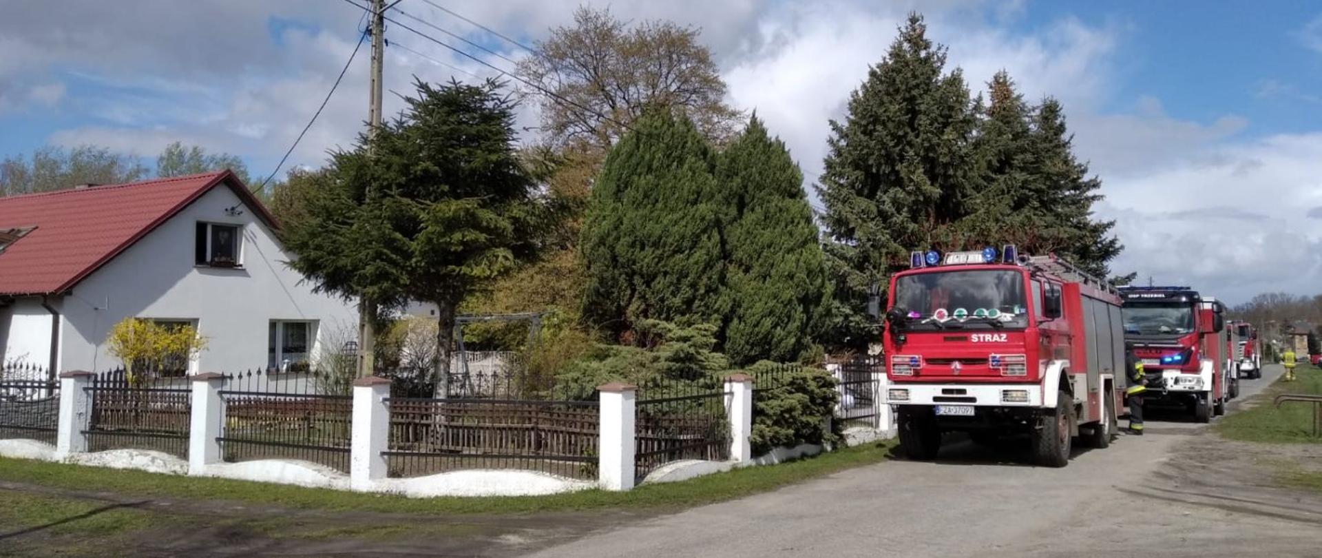 Przy budynku mieszkalnym prowadzone są działania ratowniczo- gaśnicze w miejscowości Chełmica. Na drodze zaparkowanych jest cztery samochody pożarnicze.