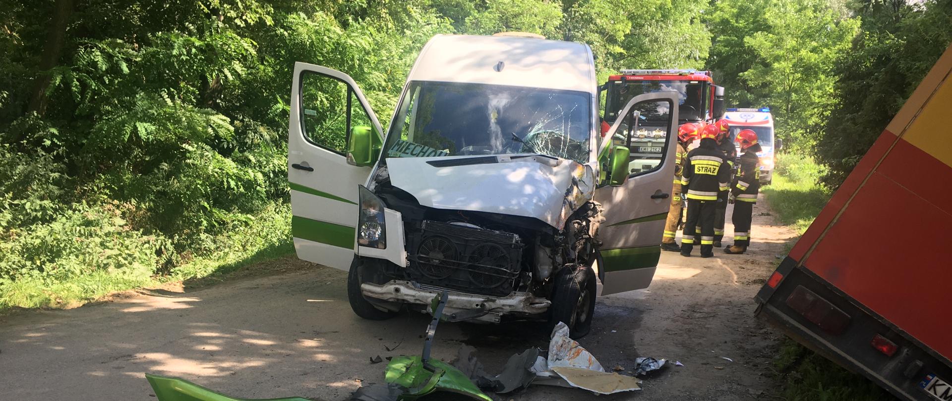 na miejscu widoczne dwa rozbite samochody ciężarowy który znajduje się w rowie oraz Bus na pasie jezdni w tle widoczni strażacy oraz pojazd Zespołu ratownictwa medycznego oraz samochód pożarniczy.