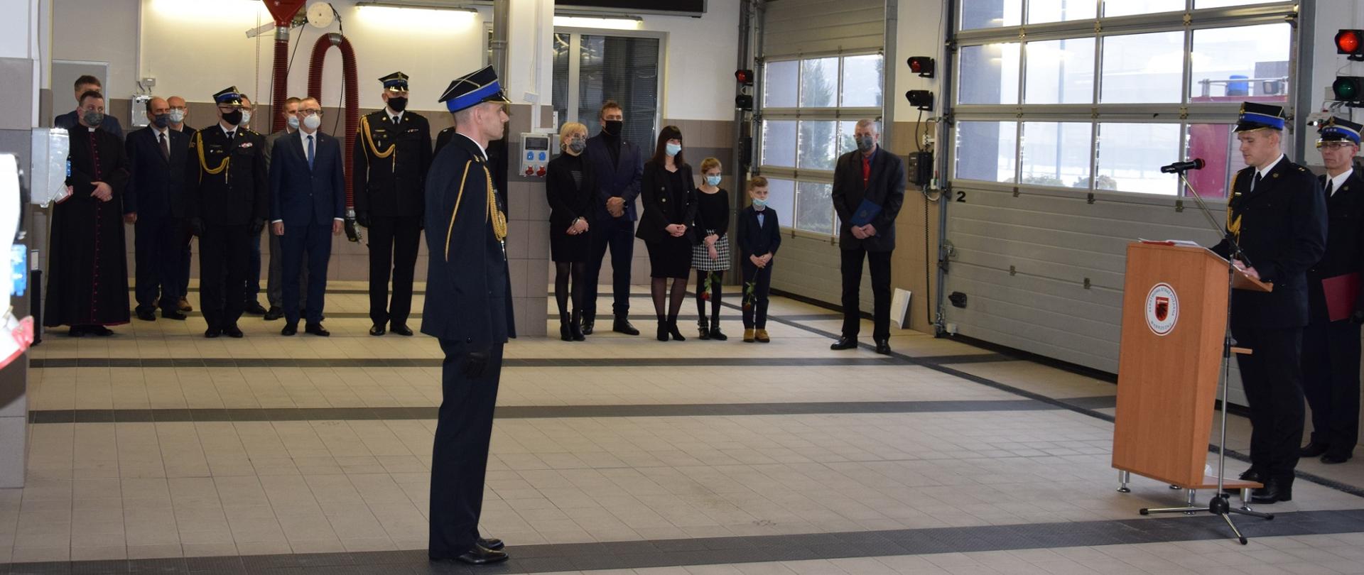 Na centralnej części zdjęcia stoi kpt. Robert Stasiak powoływany na stanowisko Zastępcy Komendanta Powiatowego Państwowej Straży Pożarnej w Wąbrzeźnie. Po prawej kpt. Karol Dzielski odczytujący treść aktu powołania, za nim stoi Komendant Powiatowy PSP w Wąbrzeźnie st.bryg. Janusz Woźniak. Na drugim planie stoją zaproszeni goście: st.bryg. Jacek Kaczmarek - Kujawsko Pomorski Komendant Wojewódzki PSP, st.bryg. Sławomir Herbowski – Zastępca Kujawsko-Pomorskiego Komendanta Wojewódzkiego PSP, Pan Krzysztof Maćkiewicz - Starosta Wąbrzeski, Burmistrz Wąbrzeźna oraz Wójtowie gmin powiatu wąbrzeskiego, dh Jarosław Herbowski – Prezes Zarządu Oddziału Powiatowego Ochotniczych Straży Pożarnych Rzeczypospolitej Polskiej w Wąbrzeźnie, ks.kan. Mariusz Stasiak – Kapelan kujawsko-pomorskich strażaków, małżonka oraz dzieci kpt. Roberta Stasiaka.