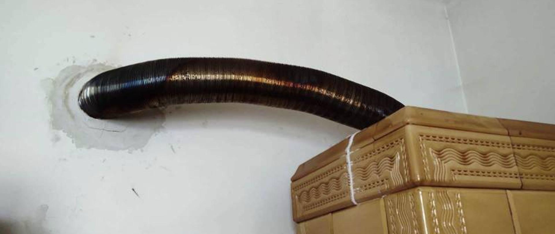 Fragment pieca kaflowego w pomieszczeniu z rozgrzaną rurą przyłączeniową do komina.