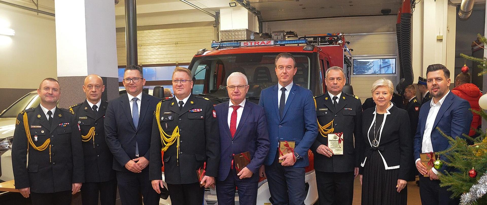 Grupa 9 osób , w tym jedna kobieta oraz 4 funkcjonariuszy PSP stoją na tle nowego samochodu rat. - gaś. pozując do zdjęcia