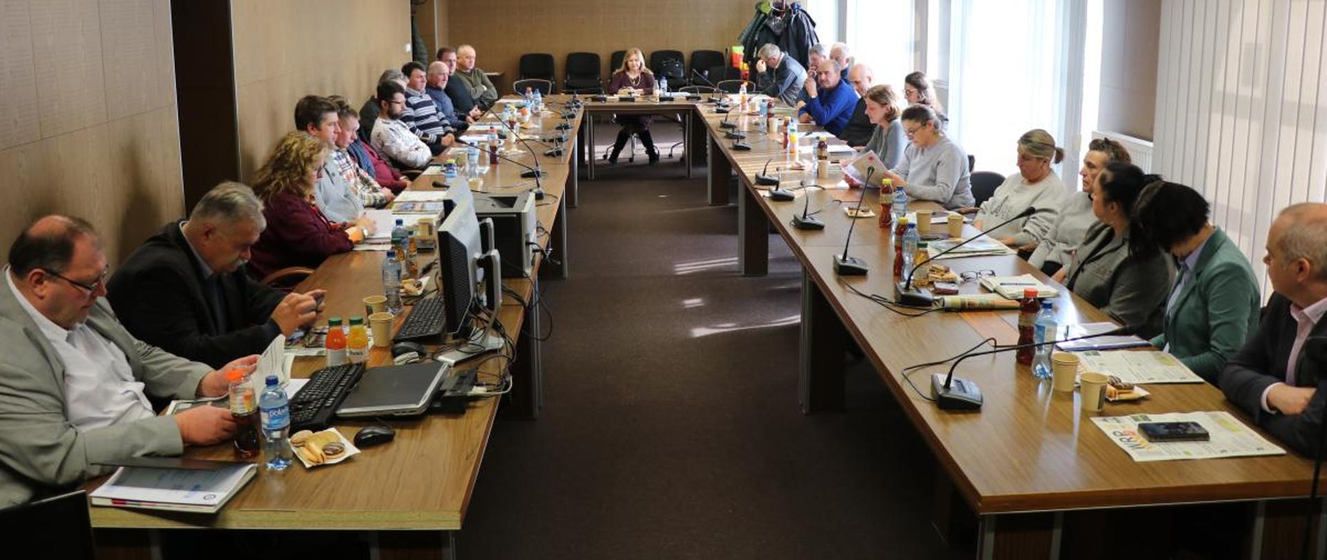 Widok sali narad i grupy osób zasiadających przy stołach