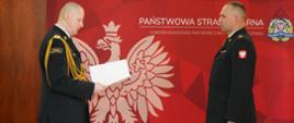 Funkcjonariusze Państwowej Straży Pożarnej w umundurowaniu na czerwonym tle z wizerunkiem godła państwowego.
