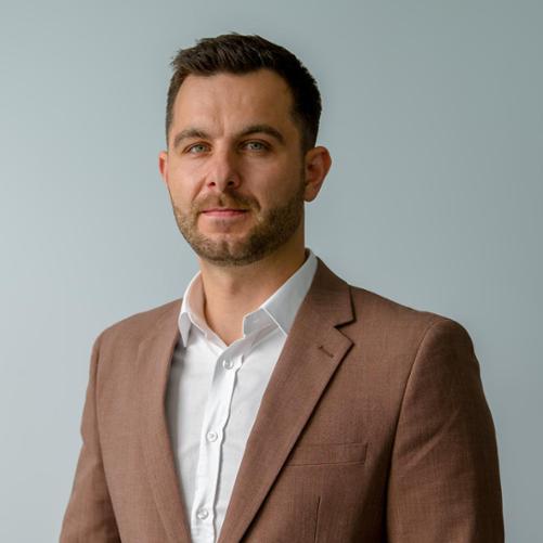 Elegancko ubrany mężczyzna w brązowym garniturze i białej koszuli.