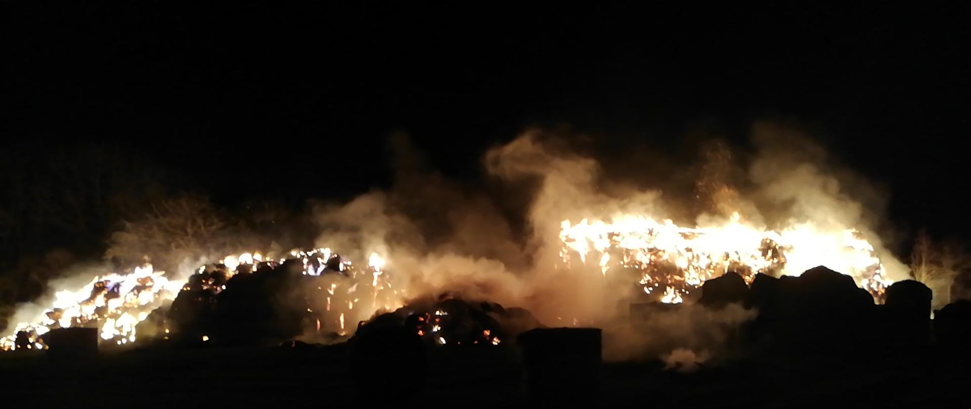 Widać pożar stogu z balotami słomy, jest noc