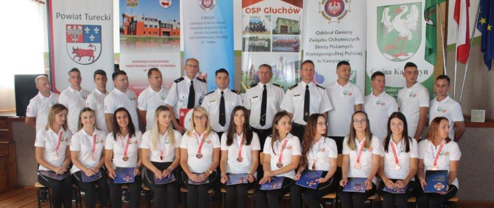 zdjecie grupowe osób , wszyscy w białych koszulach, pierwszy rząd to kobiey w białych koszulach i ciemnych spodniach, na szyi mają medale, siedzą, zdrugi rząd to mężczyźni w białych koszulach