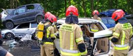 Zdjęcie przedstawia grupę strażaków podczas szkolenia podstawowego. Strażacy ćwiczą cięcie, rozpieranie elementów pojazdów. Zajęcia z tematyki: metody uwalniania osób poszkodowanych z samochodów osobowych, ciężarowych oraz autobusów – zajęcia przeprowadzane w punkcie kasacji pojazdów Eco-Auto-System w Rąbinie.