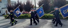 Strażacy maszerujący w trójkach ze sztandarami 