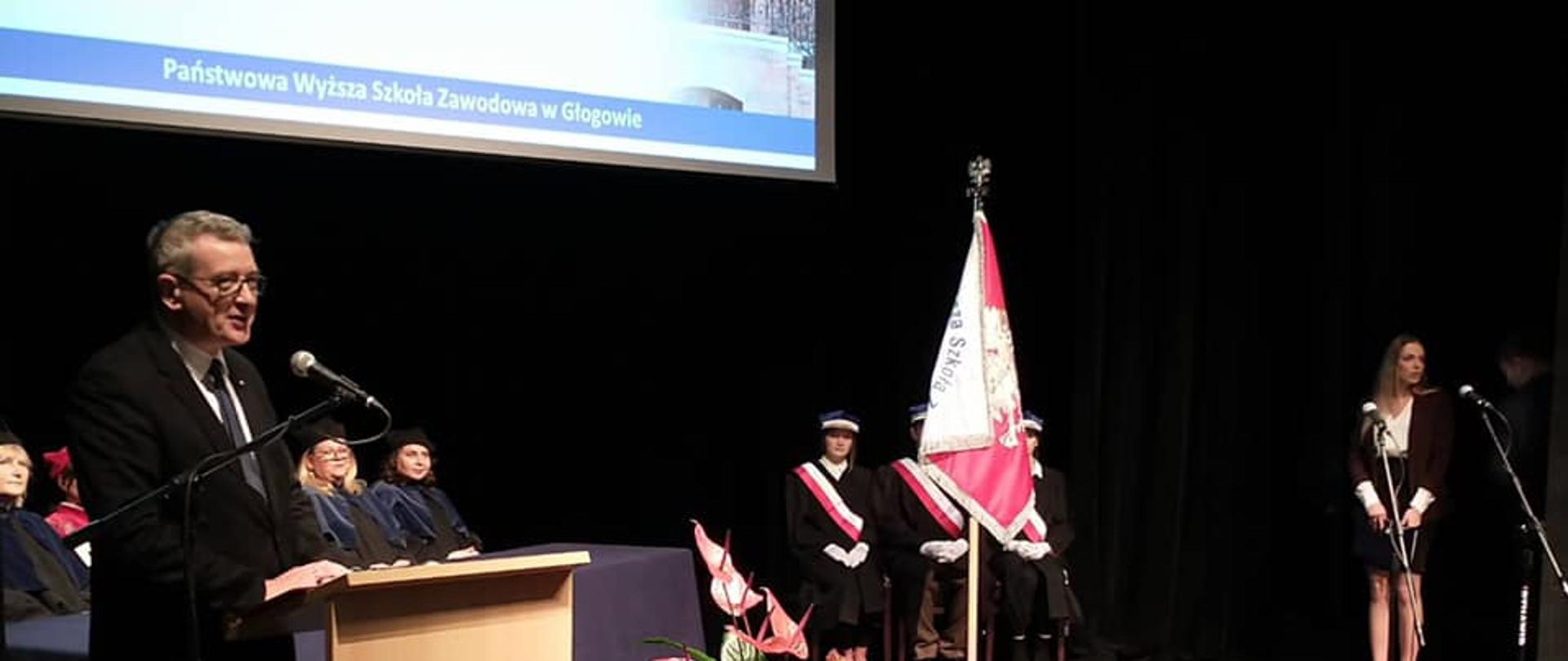 Inauguracja roku akademickiego na PWSZ w Głogowie z udziałem wiceministra Wojciecha Murdzka, wiceminister Murdzek stoi przed mównicą i przemawia, obok stoi poczet sztandarowy.